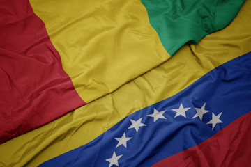 waving colorful flag of venezuela and national flag of guinea.