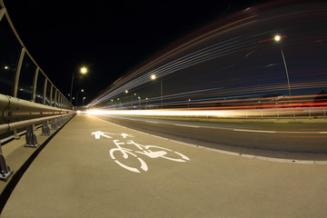Smugi światła samochodów w nocy na autostradzie, ścieżka dla roweró i pieszych.	