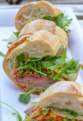 Closeup photo of a sandwich cut into three pieces on a white plate. Ingredients are slices of meat, arugula, sliced carrots and Swiss cheese. 