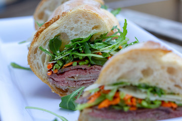 Closeup photo of a sandwich cut into three pieces on a white plate. Ingredients are slices of meat, arugula, sliced carrots and Swiss cheese. 