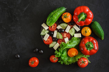 top view of a set of fresh vegetables for a greek salad whole and sliced ??on a black concrete background. creative template with space for text, logo, slogan or advertisement