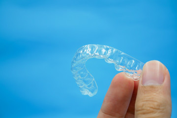 hand holding clear plastic retainer teeth that isolated on blue sky background. it's an equipment for orthodontist give the patient to orthodontic surgery in dental clinic or hospital