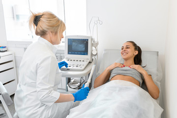 The gynecologist sets up the ultrasound machine and explains to the patient how the study will be performed. Ultrasound of the pelvic organs - obrazy, fototapety, plakaty