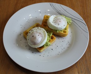 2 poached eggs on a bed of avocado placed onto potato waffles, with a smattering of black pepper
