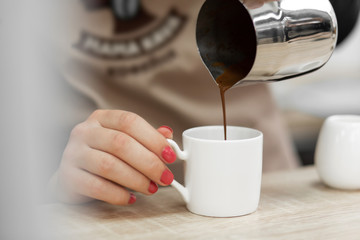 An apron barista pours hot cocoa into a cup. Barista work in a coffee shop