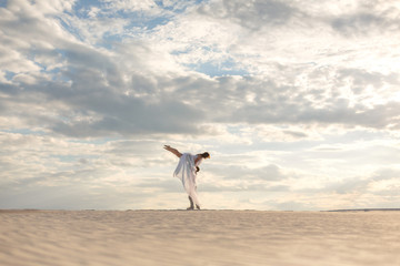 Romantic couple dancing in sand desert. The guy lifts the girl above himself. Sunset sky.