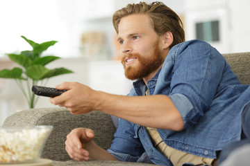 bachelor layed on sofa changing channel with remote control