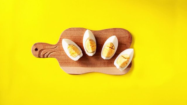 Stop motion animation of one white egg on a wooden cutting board is cut into halves then into quarters, which then represent a smile on yellow background - Powered by Adobe