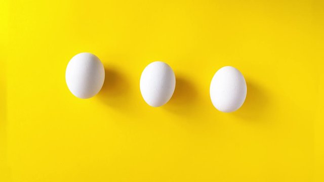 Stop motion animation of three white eggs running on a yellow background and draw an infinity sign. 