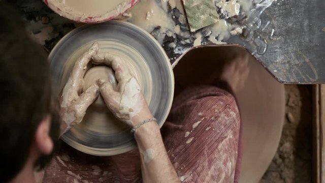 The potter makes a jug of clay. Ceramist. A man makes a vase on a potter's wheel. Hands of the master turn a piece of clay into a jug. Handwork. Pottery. Sculptor's wet hands close up.  Clay dishes