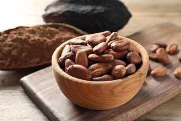 Wooden bowl with cocoa beans on table