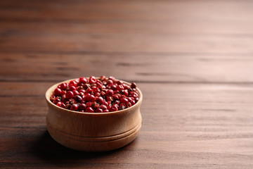 Bowl of red pepper corns on wooden table, space for text
