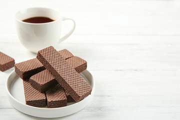Plate of delicious chocolate wafers with cup of tea on white wooden background. Space for text