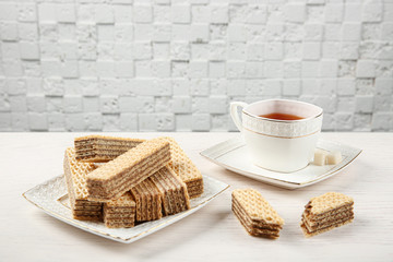 Plate of delicious wafers with cup of tea on white wooden table