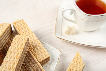 Plate of delicious wafers with cup of tea on white wooden background, closeup