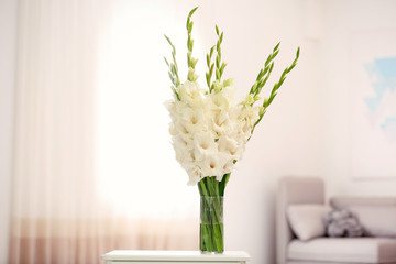 Vase with beautiful white gladiolus flowers on wooden table in room, space for text