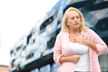 Mature woman suffering from heart attack outdoors. Space for text