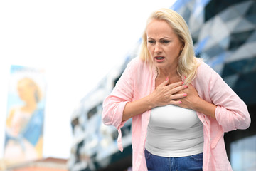 Mature woman suffering from heart attack outdoors. Space for text