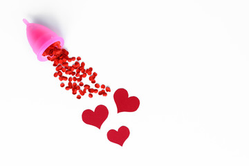 Top view of pink menstrual cup filled with red confetti imitate flow blood and red hearts, on white background with copy space. Concept of love your body.