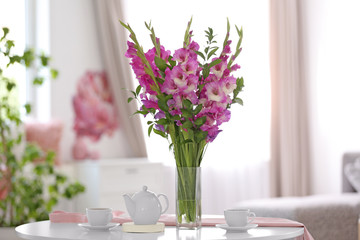 Vase with beautiful pink gladiolus flowers on wooden table in living room