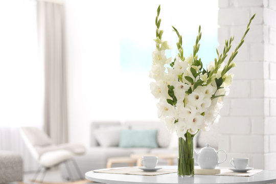 Vase with beautiful white gladiolus flowers on wooden table in living room. Space for text