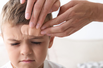 Woman applying adhesive bandage on boy's forehead indoors, closeup