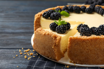 Sliced delicious cheesecake with blackberries on wooden table, closeup