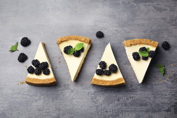 Pieces of delicious cheesecake with blackberries on grey background, flat lay