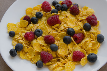 Corn flakes with fresh raspberries and blueberries in a white plate
