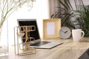 Stylish workplace interior with jewelry holder on wooden table near window. Space for text