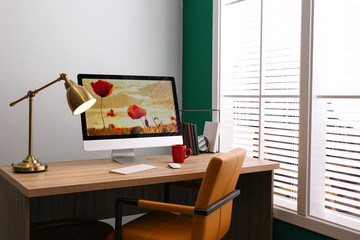 Comfortable workplace near window with white horizontal blinds in room