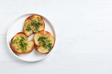 Slices of toasted bread with garlic and herb on white wooden table, top view. Space for text