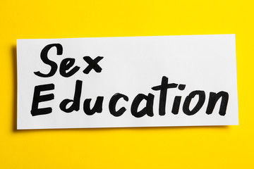 Piece of paper with phrase "SEX EDUCATION" on yellow background, top view