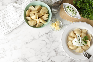 Delicious cooked dumplings with sour cream on white marble table, flat lay. Space for text