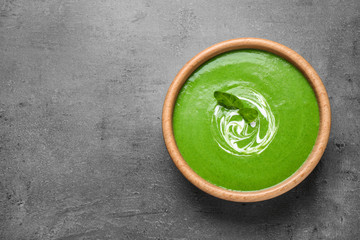 Bowl of healthy green soup with fresh spinach on grey table, top view. Space for text