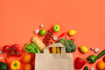 Paper bag with different groceries on coral background, flat lay