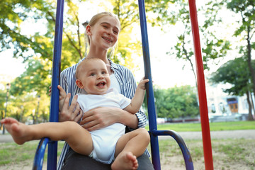 Teen nanny with cute little baby on swing outdoors