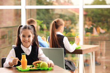 Happy girl at table with healthy food in school canteen