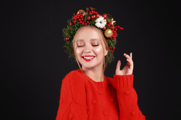 Beautiful young woman wearing Christmas wreath on black background
