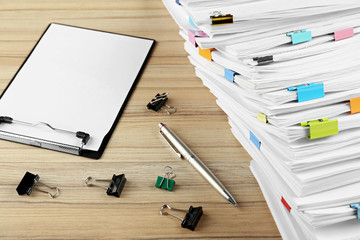 Stack of documents with binder clips, clipboard and pen on wooden table