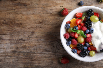 Fresh tasty fruit salad with yogurt on wooden table, flat lay. Space for text