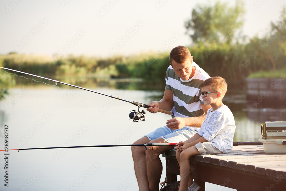 Wall mural Dad and son fishing together on sunny day