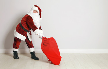 Authentic Santa Claus with bag full of gifts against grey wall. Space for text