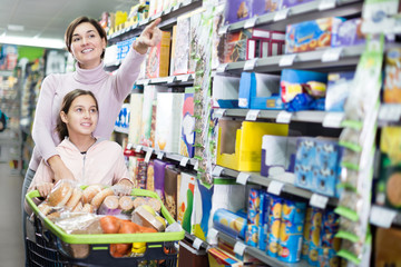 Woman with girl looking for food in supermarket