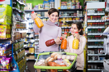 smiling mother with daughter choosing refreshing beverages in supermarket
