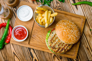 Burger with chicken and fries with sause on the board