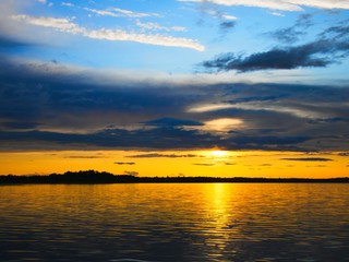 Setting sun hides behind clouds in beautiful sunset in blue and gold over Lake Irving in Bemidji Minnesota on a summer evening.