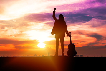 Silhouette traveler young women musician holding guitar and her hand while standing on sunset background with copy space. Beautiful sky sunrise with young girl feeling freedom with acoustic guitar.