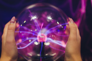 Hand touching a plasma ball with smooth magenta-blue flames.