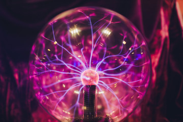 Hand touching a plasma ball with smooth magenta-blue flames.
